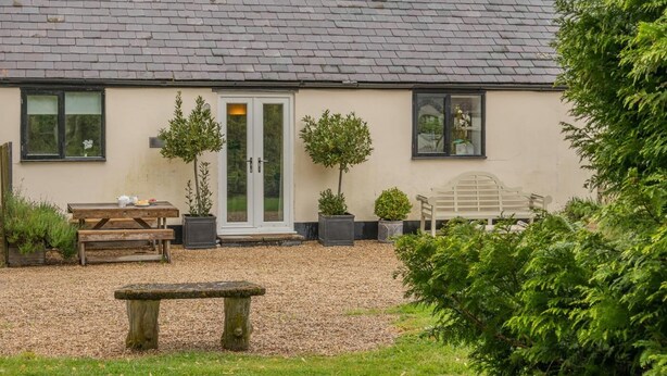 A building with a tiled roof, a front door with glass panels, a bench, and potted plants. - 2 Bed in Shaftesbury (oc-28678) (Sedgehill)