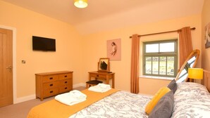 Um quarto com uma cama, cômoda, televisão, janela com cortinas e um quadro na parede.
