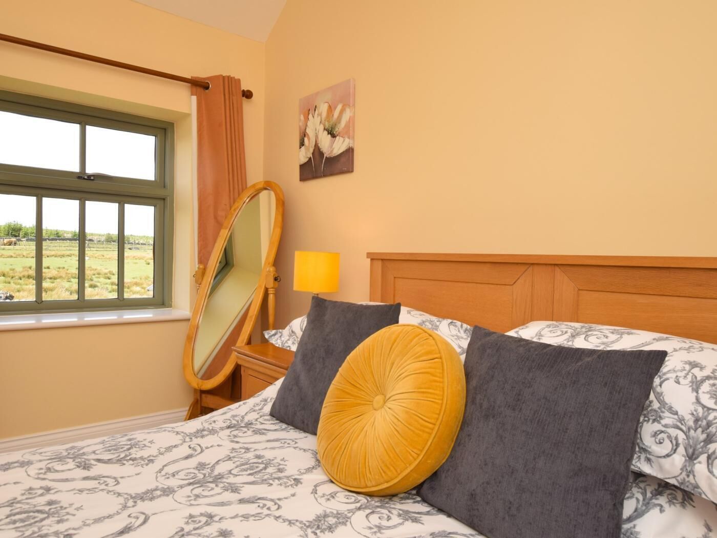 Une chambre à coucher avec un lit, un miroir, une lampe et un tableau accroché au mur.