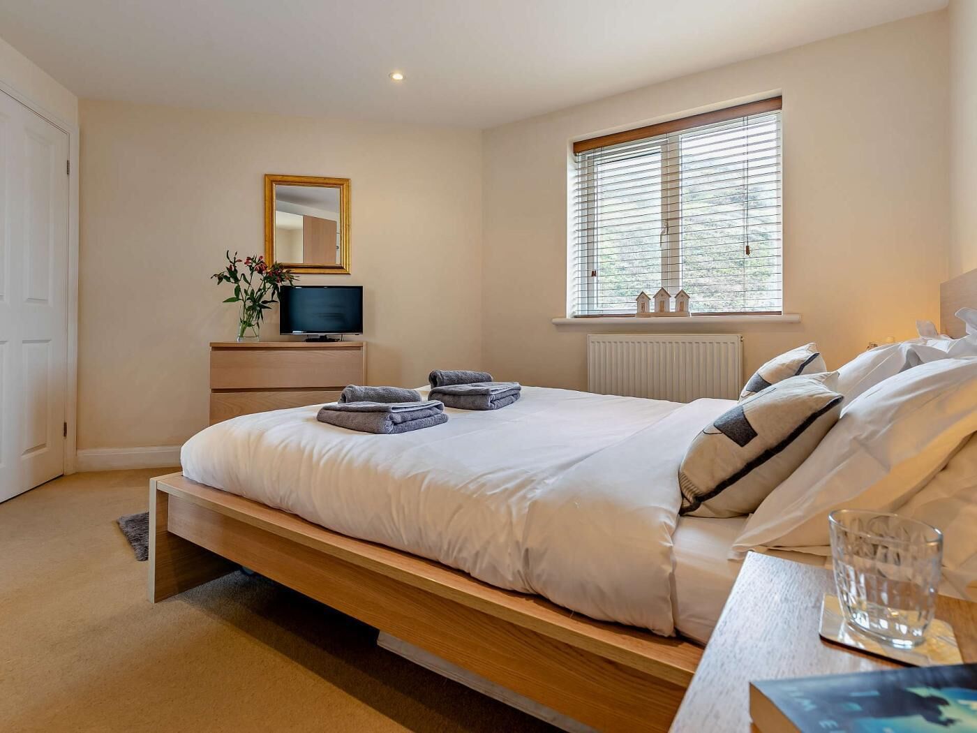 A bedroom with a bed, bedside table, TV, window, and a mirror.