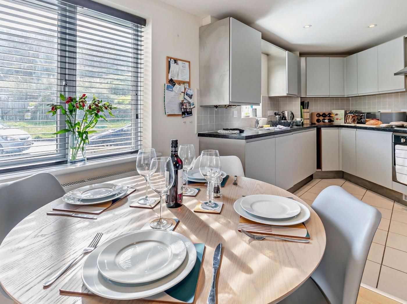 Une cuisine moderne avec des meubles blancs, un coin repas doté d’une table ronde pour quatre personnes, et une vue sur l’extérieur grâce à de grandes fenêtres.
