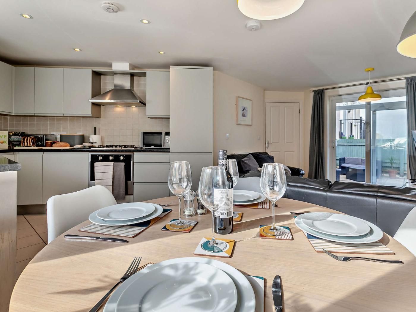 A modern kitchen with white cabinets, a stove, and a dining area set for four with plates, glasses, and cutlery.