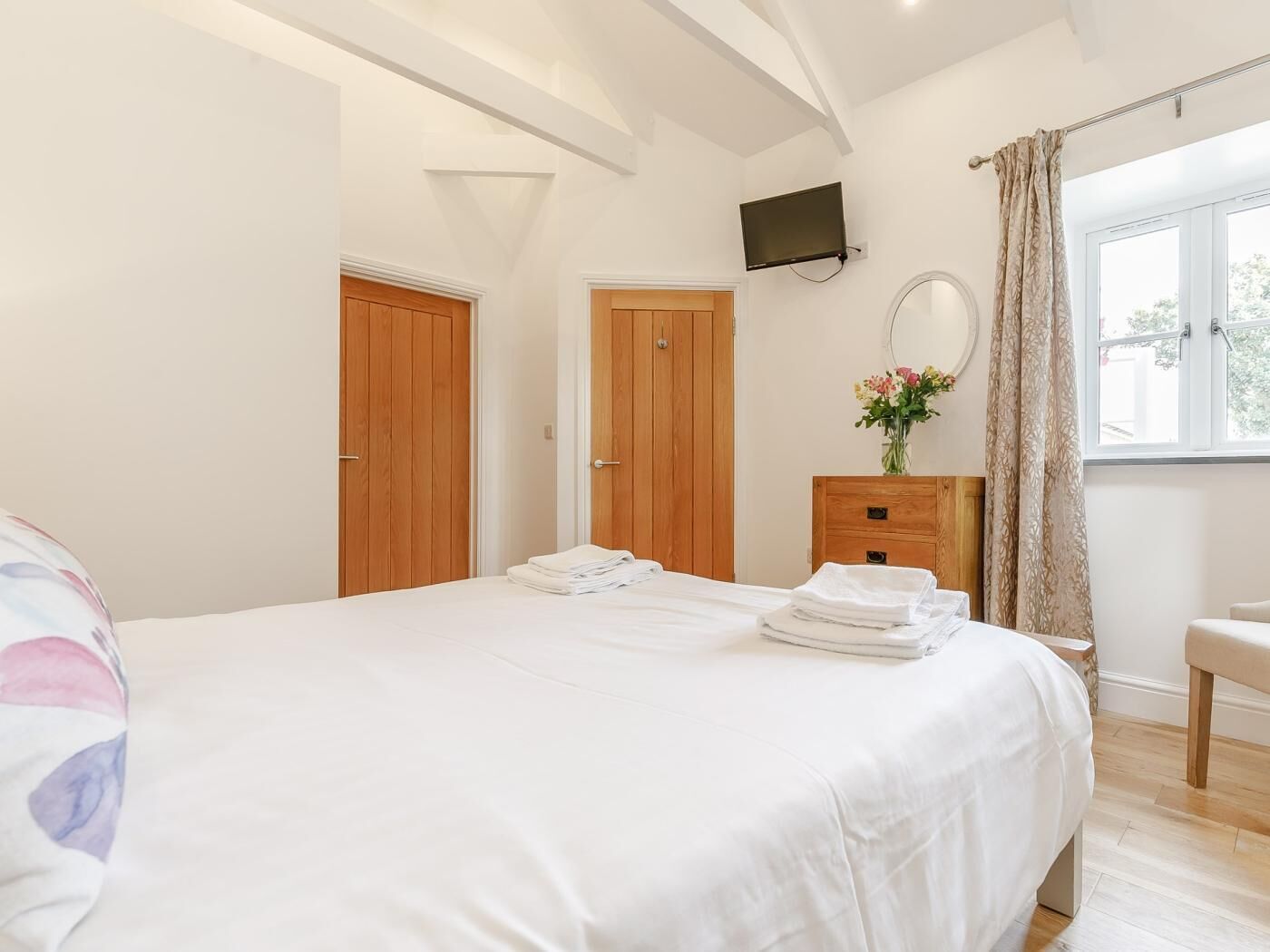 Une chambre à coucher avec un lit, des portes en bois, un téléviseur, une commode et une fenêtre avec des rideaux.