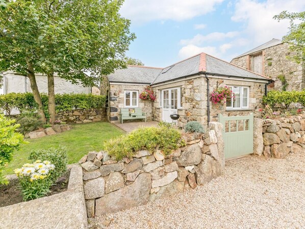 Une petite maison en pierre avec un jardin, un banc et un mur en pierre.