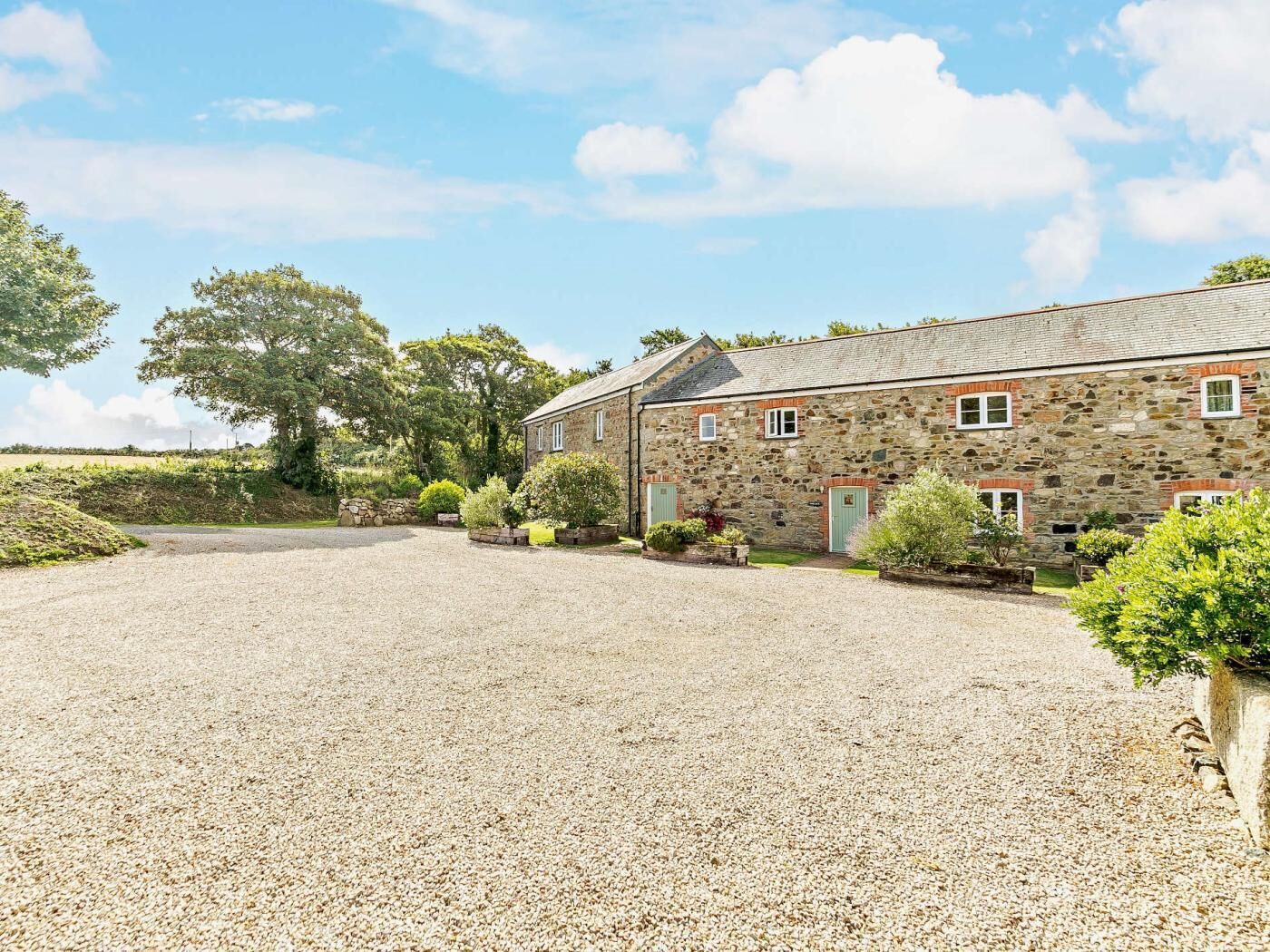 A stone building with a gravel driveway and surrounding greenery.