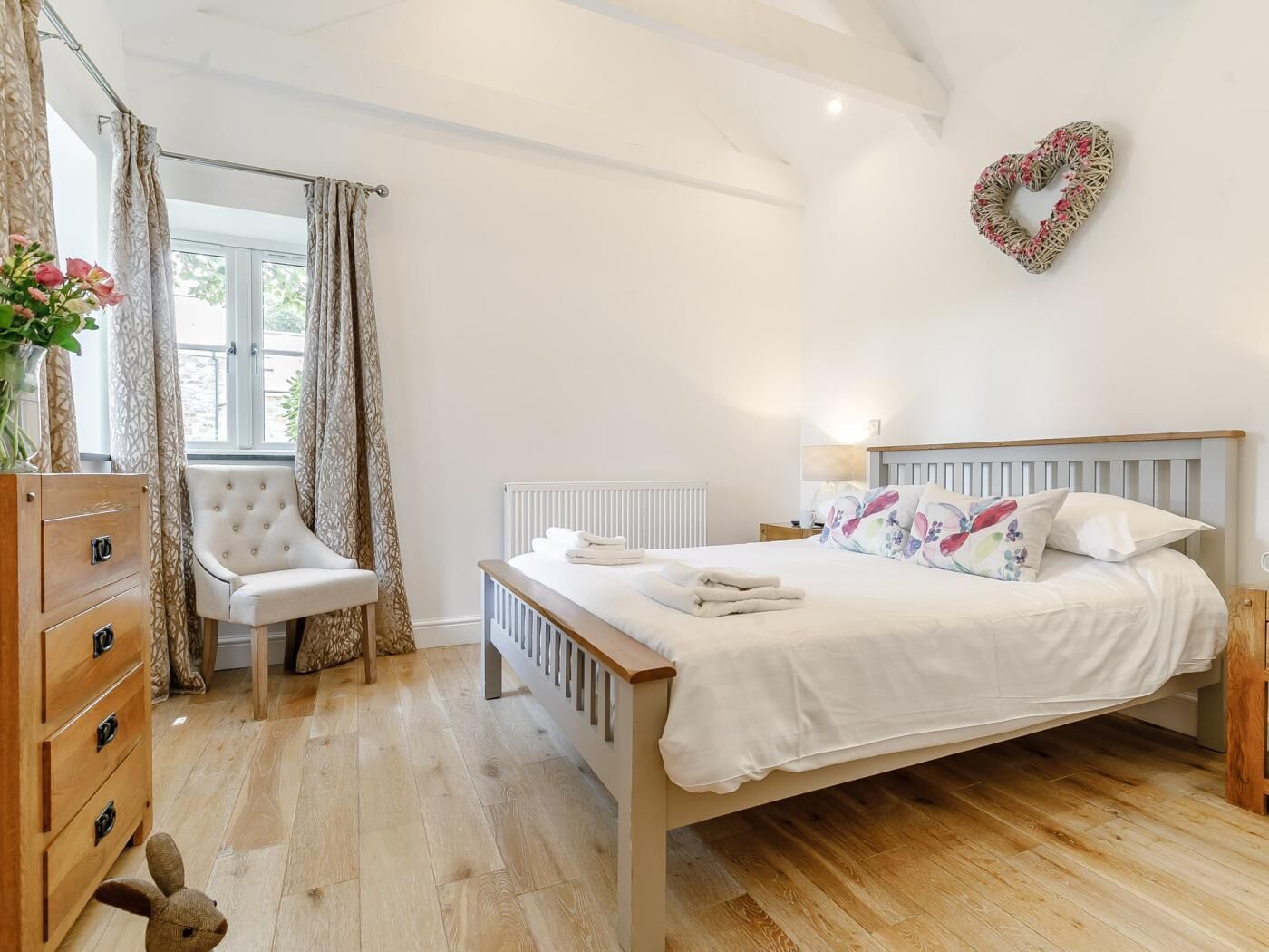 A bedroom with a wooden bed, a chair, a dresser, and a window with curtains.