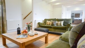 Un salon avec une table basse en bois, un canapé vert et une cuisine en arrière-plan.