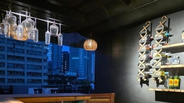 A bar with a wooden counter, hanging glassware, and shelves with bottles. - The CRADLE (Dar es Salaam)