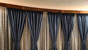 A bedroom with a wooden ceiling, a bed with a quilted mattress, and curtains with a geometric pattern. - The CRADLE (Dar es Salaam)