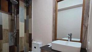 A bathroom with a toilet, sink, mirror, and shower. - The CRADLE (Dar es Salaam)