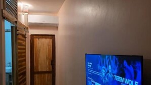 A hallway with a wall-mounted TV displaying 'TEEN WOLF' and a wooden door at the end. - The CRADLE (Dar es Salaam)