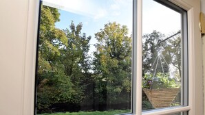 Ein Fenster mit Blick auf einen Garten, einem hängenden Korb und einer Metallkonstruktion.