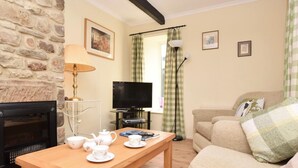 Ein gemütliches Wohnzimmer mit Kamin, Fernseher, Sofa und einem Tisch mit Teeservice.