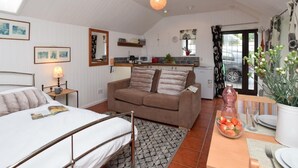 A compact room with a bed, a sofa, a dining table with a bowl of fruit, a kitchen area, and a window with curtains. - 1 Bed in Launceston (oc-36500) (Egloskerry)
