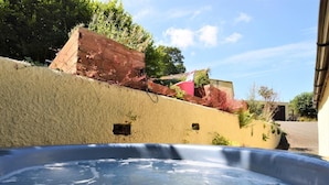 A hot tub in a backyard with a beige wall, a red brick structure, and a pink building in the background. - 1 Bed in Launceston (oc-36500) (Egloskerry)