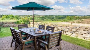 Une terrasse extérieure avec une table et des chaises, un parasol vert et une vue pittoresque sur la campagne.