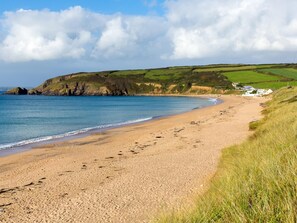 A coastal beach with a sandy shore, grassy areas, and a cliff in the background. - 3 Bed in Penzance (oc-36258) (Trescowe)