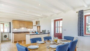 Une cuisine moderne avec des meubles en bois, un îlot central et un coin repas comprenant des chaises bleues et une table en bois.