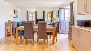 Een eethoek met een houten tafel en stoelen, een televisie, en een keukenhoek met kastjes en een magnetron.