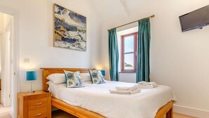 Een slaapkamer met een houten bed, een nachtkastje, een lamp, een schilderij en een raam met gordijnen.