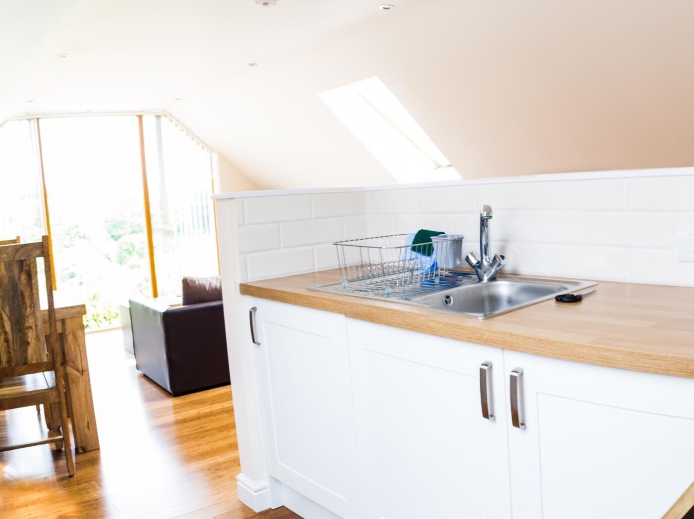 A modern kitchen with white cabinets, a wooden countertop, a stainless steel sink, and a dish rack.