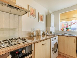 A kitchen with a gas stove, oven, washing machine, and a window with a view.