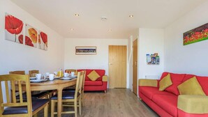 Une pièce avec une table à manger dressée pour quatre personnes, un canapé rouge, des chaises en bois et une porte donnant sur une autre pièce.