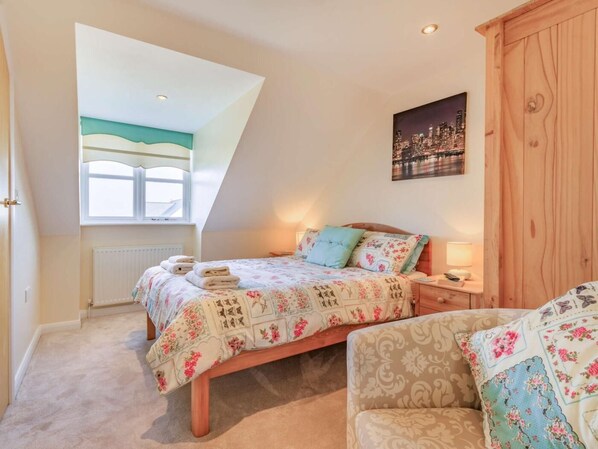 A bedroom with a bed, a nightstand, a chair, a window, and a cityscape painting.