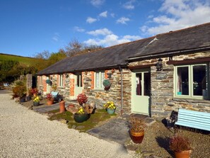 A stone cottage with a green door, potted plants, and a bench outside. - 1 Bed in Tintagel (oc-36928) (Tintagel)
