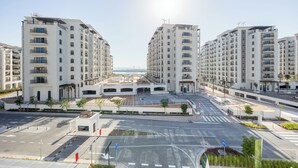 A modern apartment complex with multiple high-rise buildings, a central pedestrian area, and a clear view of the sea in the background. - Bloomfields 1BR in Yas Golf Collection  (Abu Dhabi)