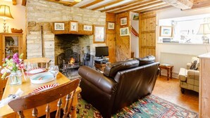 A rustic living room with exposed wooden beams, a stone fireplace, a leather sofa, and a dining table set with plates and glasses. - 2 Bed in Lechlade (oc-40192) (Langford)