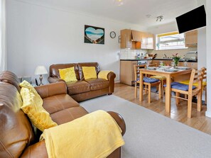 A living room with a brown leather sofa, a dining table with chairs, a kitchen area, and a heart-shaped artwork on the wall. - 2 Bed in Helston (oc-36430) (Mullion)