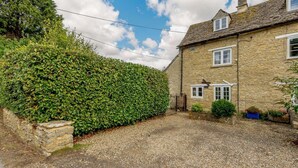 Une maison en pierre avec une allée gravillonnée et une haie bien entretenue.