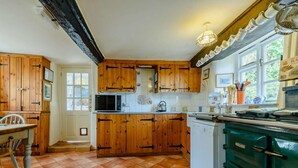 Une cuisine avec des meubles en bois, un four à micro-ondes, une bouilloire et un poêle vert.