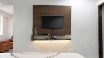 Habitación de hotel moderna con una televisión de pantalla plana montada, un estante de madera debajo y una cama con una colcha blanca.
