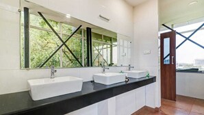 A modern bathroom with two sinks, a large mirror, and a view of greenery through the windows. - Hotel Southgate (Thiruvananthapuram)