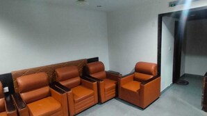 A room with a sectional sofa and a single chair, a door, and a red curtain. - Hotel Southgate (Thiruvananthapuram)