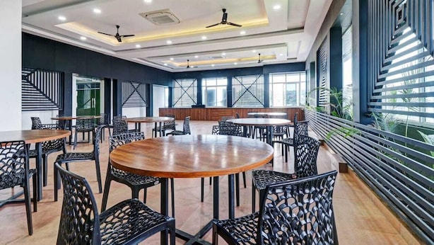 A conference room with round tables, black chairs, and a modern ceiling design. - Hotel Southgate (Thiruvananthapuram)