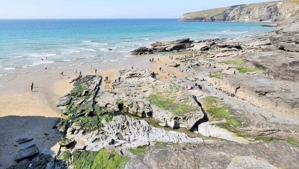 Una playa rocosa con aguas cristalinas y un acantilado al fondo.