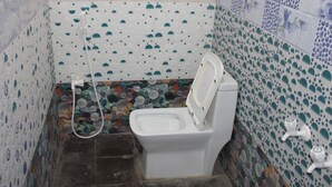A small bathroom with a toilet, a shower, and a tiled wall with a pattern of circles and semi-circles. - sri sakthivel santhamurugan residency (Tiruvannamalai)