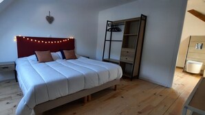 A bedroom with a sloped ceiling, a bed with white bedding, a bedside table, a wardrobe, and a heart-shaped wall decoration. - Large, renovated house in central Alsace (130 m²) (Neubois)