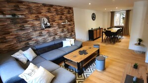 A modern living room with a sectional sofa, a wooden coffee table, and a dining area with a table and chairs. - Large, renovated house in central Alsace (130 m²) (Neubois)