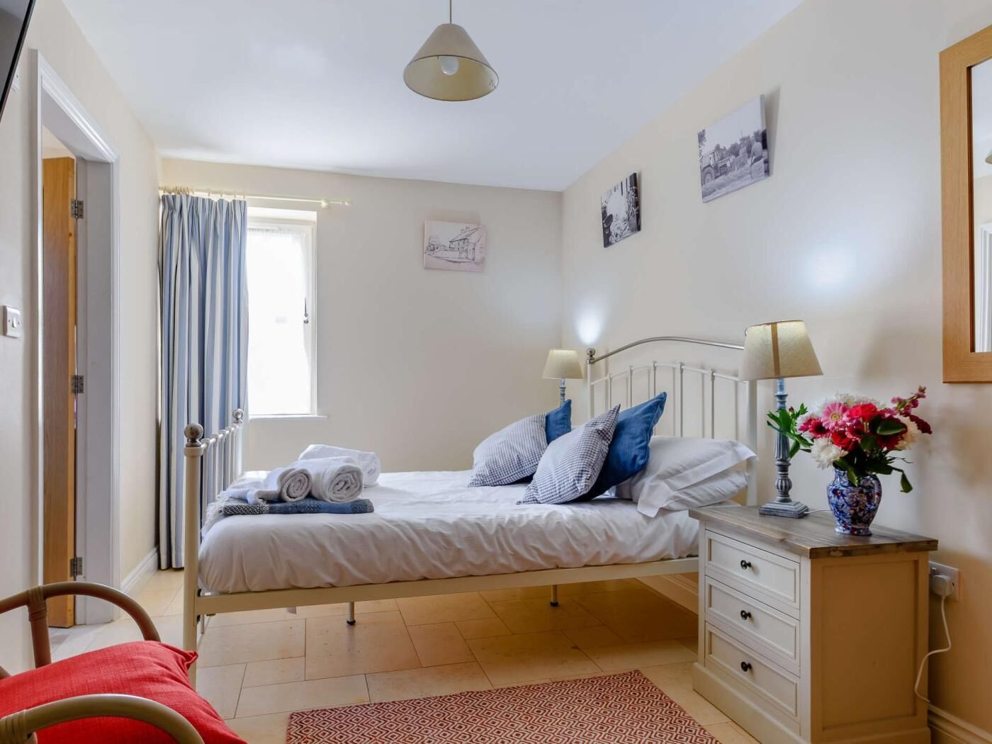 A bedroom with a bed, bedside tables, a dresser, a window with curtains, and wall art.