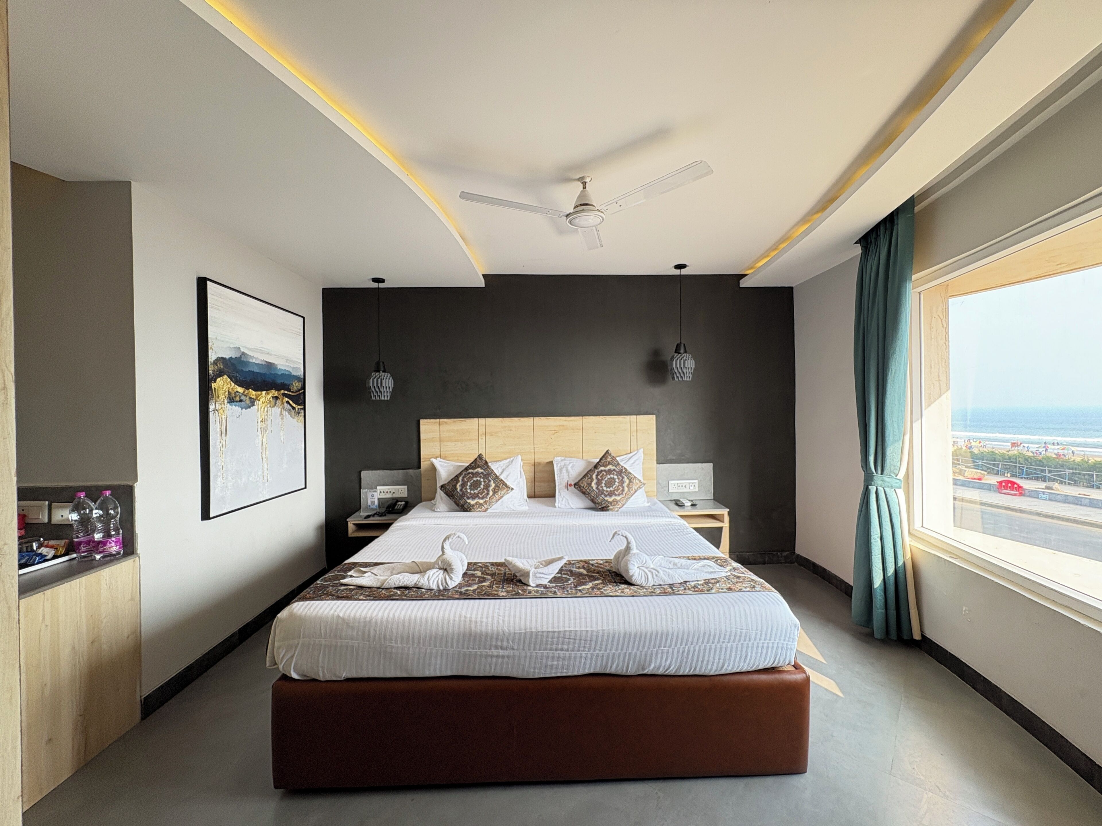 Une chambre d’hôtel moderne dotée d’un grand lit, d’un ventilateur de plafond, d’une vue sur la mer et d’une tête de lit en bois.