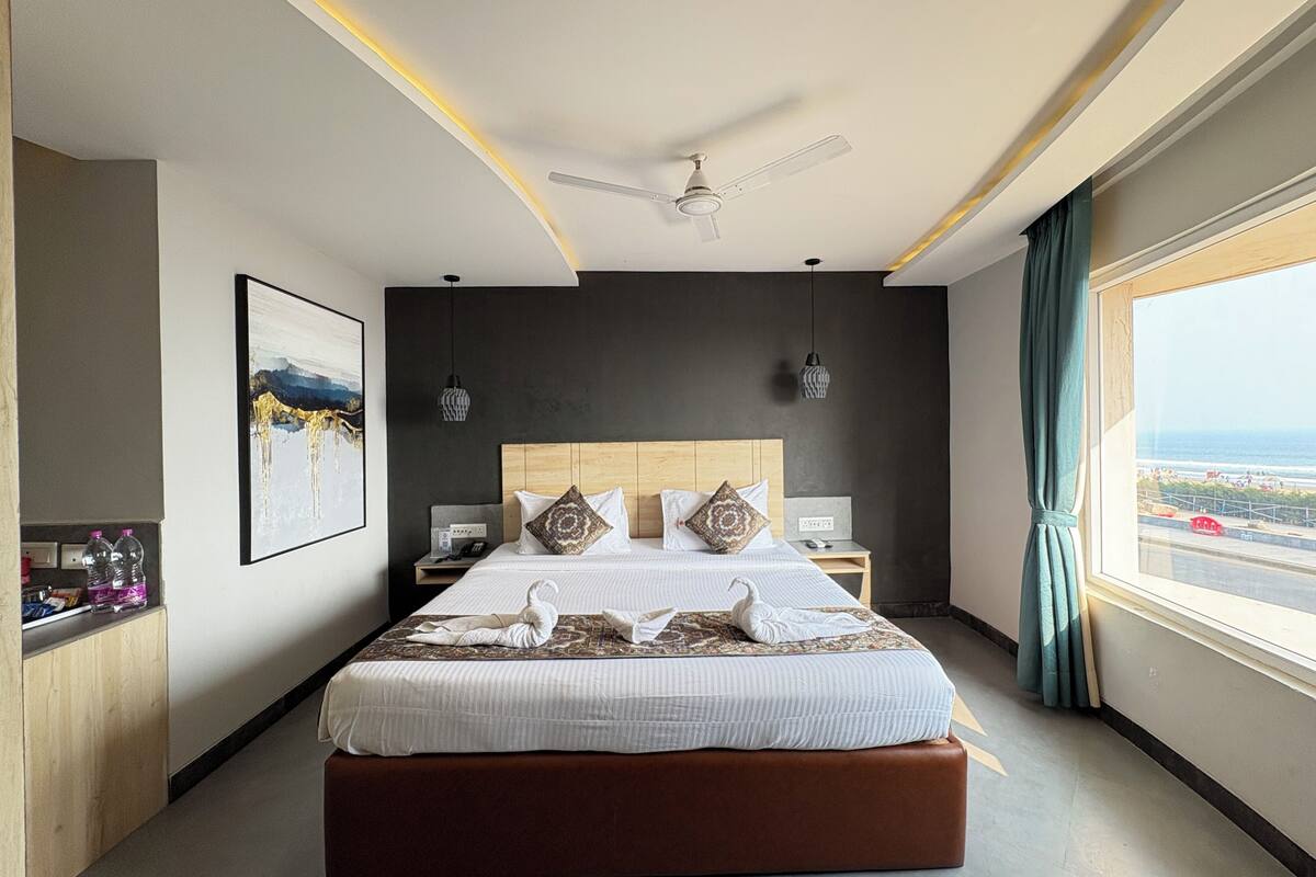 A modern hotel room with a large bed, a ceiling fan, a view of the sea, and a wooden headboard.