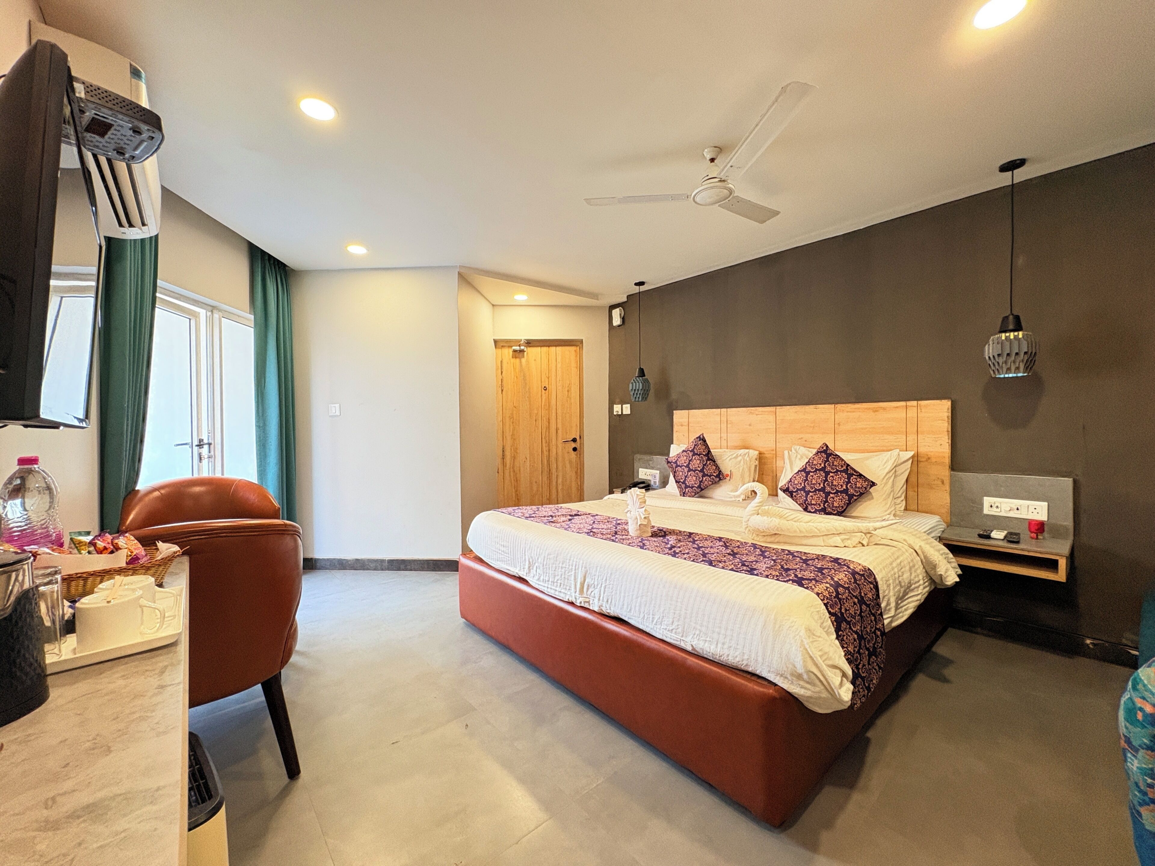 Une chambre d’hôtel moderne dotée d’un grand lit, d’un bureau avec une chaise, d’un ventilateur de plafond et d’une table de chevet avec une lampe.