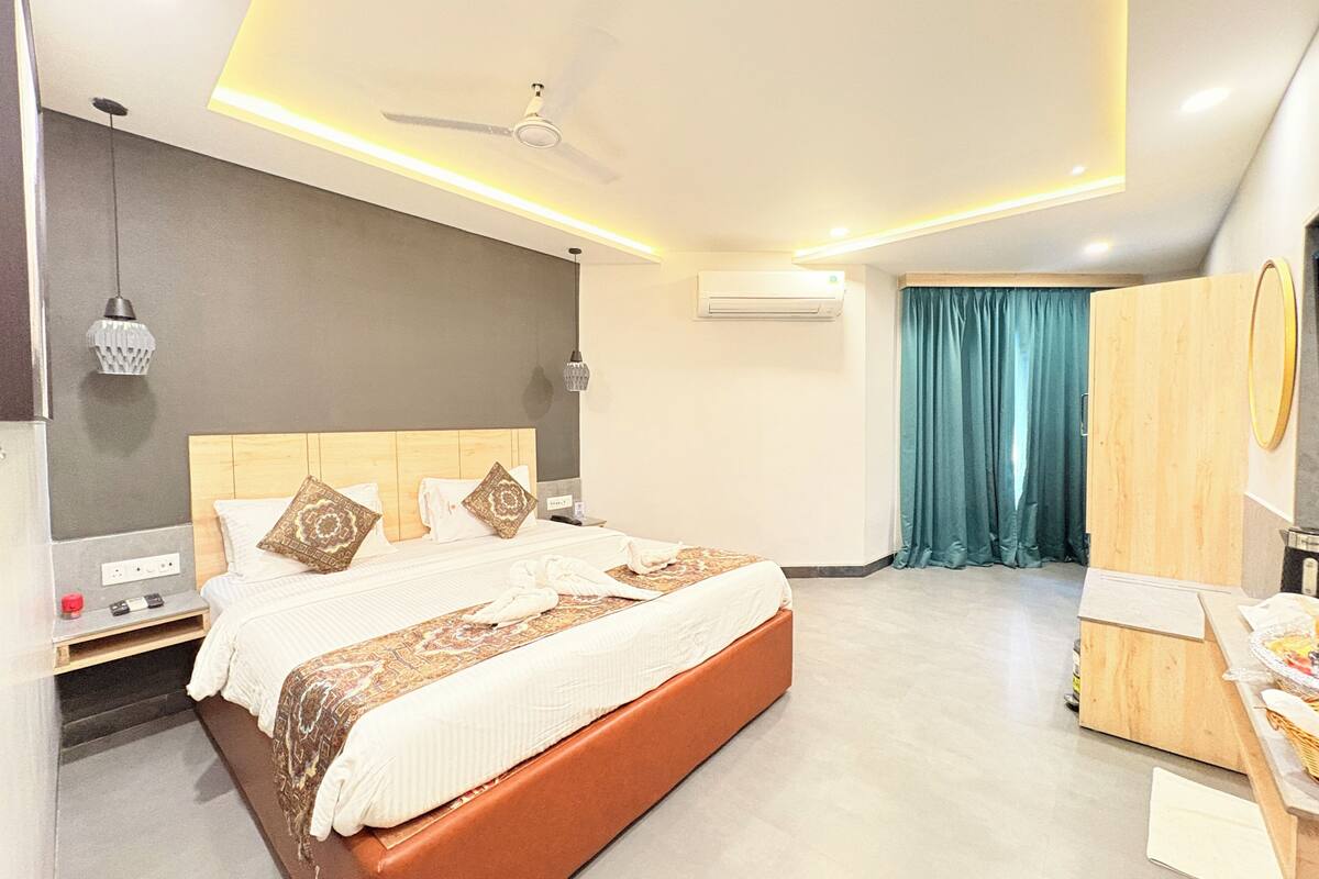 A modern hotel room with a large bed, a ceiling fan, an air conditioning unit, a vanity with a mirror, and a wardrobe.