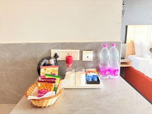 A hotel room with a breakfast tray, a basket of snacks, two water bottles, and a coffee maker. - Hotel on New Marine Drive Rd. Prabhupada (Puri)