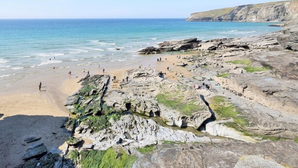 Una playa rocosa con aguas cristalinas y un acantilado al fondo.