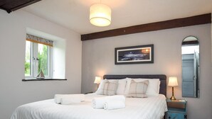 Une chambre à coucher avec un lit, deux lampes de chevet, un tableau encadré, une fenêtre décorée d’un motif de voilier et une porte.